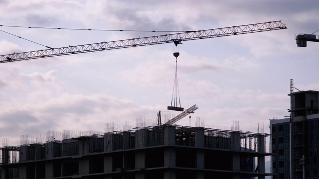 建筑工地上的塔式起重机在高层建筑中吊装重物视频素材