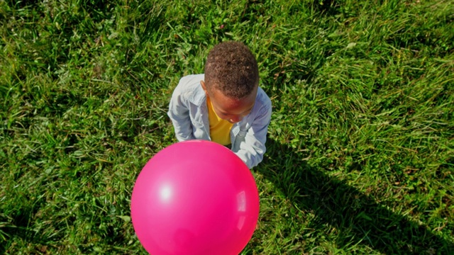 SLO MO CS小男孩在阳光明媚的草地上拿着一个粉红色的气球视频素材