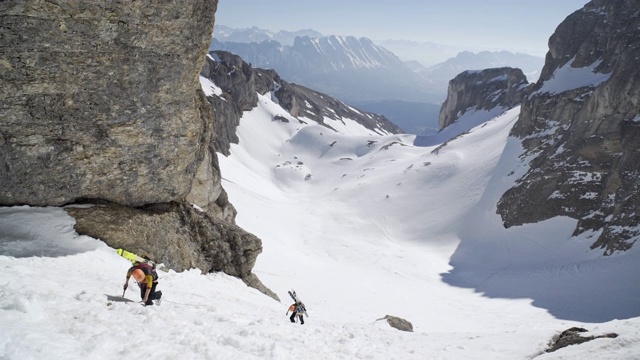 登山者在雪地里用绳子爬山，背包上放着滑雪板。视频下载