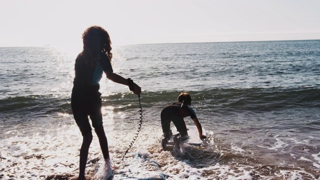 两个剪影的孩子穿着潜水服和冲浪板在夏天的海滩度假视频下载