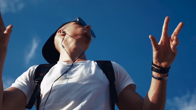 年轻人戴着耳机在天空背景上跳舞视频素材