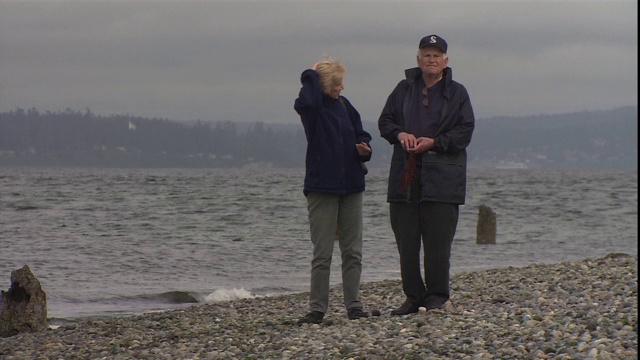 一对老夫妇沿着布满卵石的海岸漫步。视频下载
