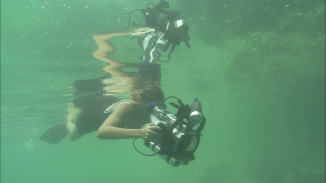一位摄影师带着水下照相机在海面下游泳。视频下载