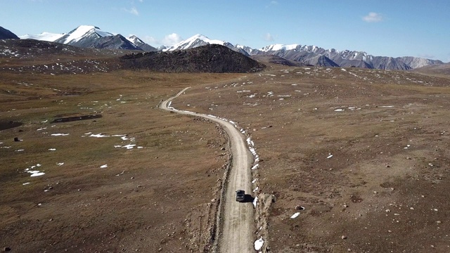 无人机拍摄的丰田4Runner带着车顶的盒子沿着蜿蜒的砾石路行驶，穿越远处壮观的雪山景观。视频下载