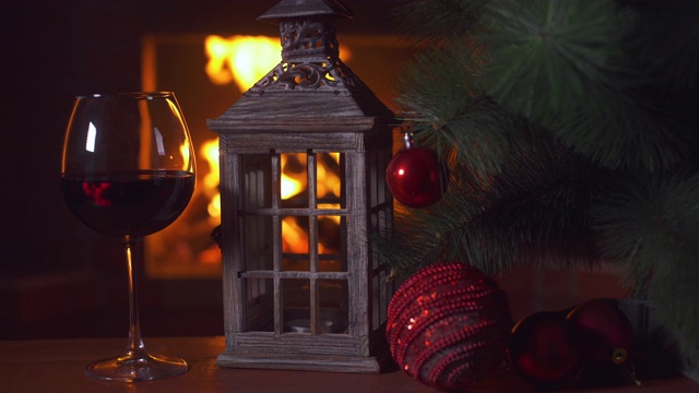 桌上放着一杯红酒，一盏圣诞灯和一棵圣诞树。背景-壁炉与火焰。新年假期酗酒。酒精饮料。火的背景。独自喝。餐厅的饮料视频下载