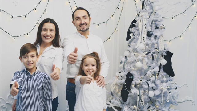 慈爱的父母和孩子们站在圣诞树旁，摆姿势，竖起大拇指。视频下载