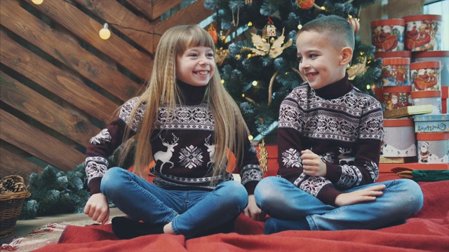 甜蜜的孩子们在彼此的耳朵里窃窃私语着秘密，坐在家里的红毯上，庆祝圣诞节。视频素材