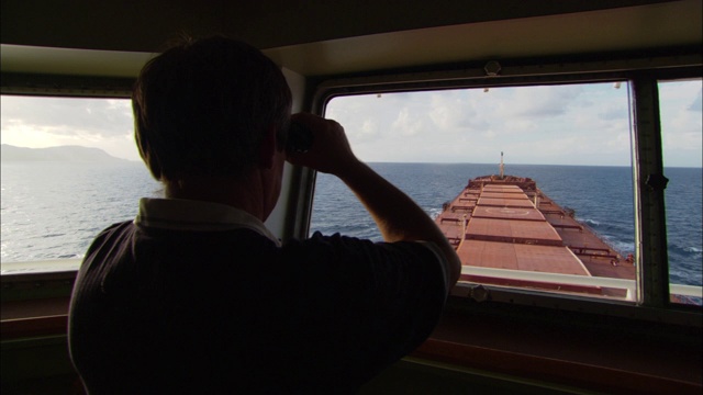 一艘驳船的船长透过双筒望远镜望着桥上的窗户。视频下载