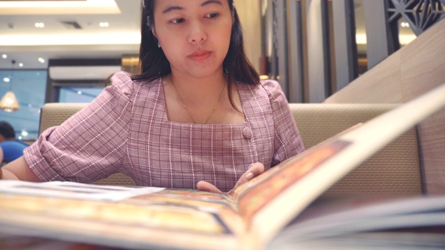 年轻亚洲女人在餐厅看菜单的慢镜头，假期周末的概念，亚洲女人的生活方式视频素材