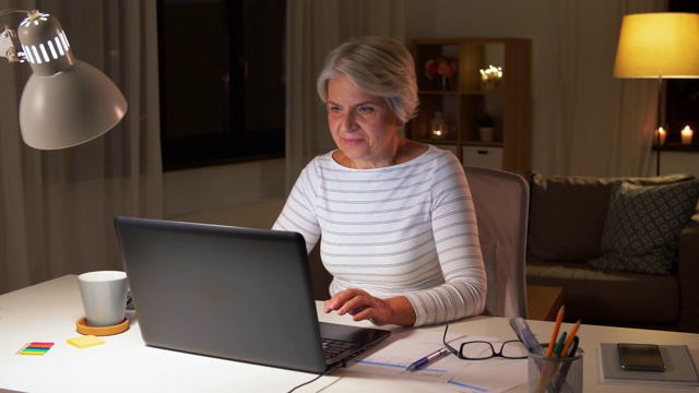 快乐的老女人晚上在家用笔记本电脑视频素材