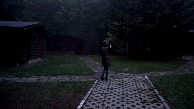 孤独迷失的女孩带着手机在废弃的小木屋间行走，寻找信号视频素材