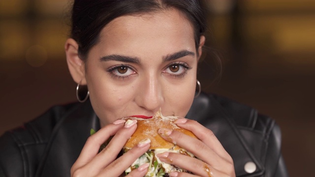 一个美丽的年轻女人的特写镜头与红色的嘴唇吃大新鲜烹制的汉堡包与快乐在快餐店。美国街头小吃的概念。视频素材