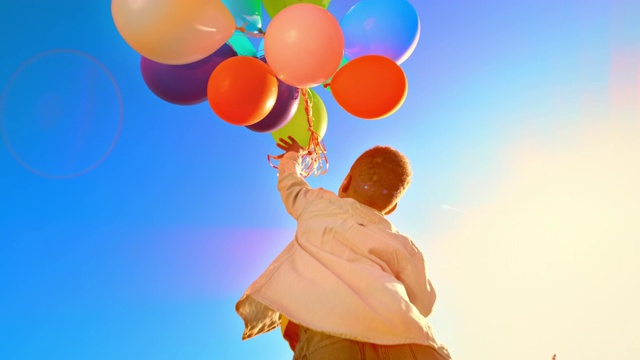 SLO MO Boy跳起来，把一堆五颜六色的气球放飞到空中视频素材