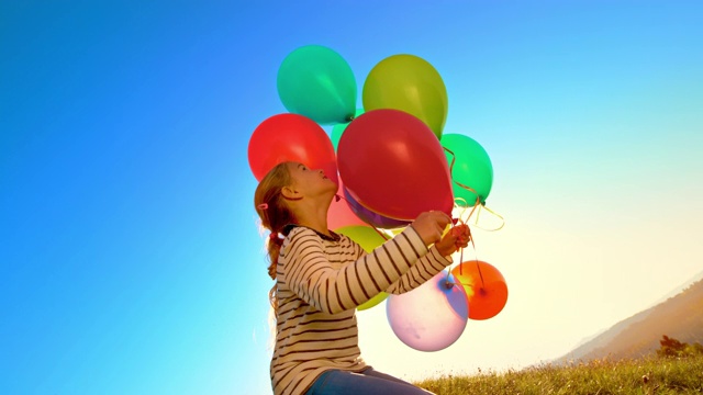 SLO MO女孩在一个阳光明媚的日子里向空中放飞五颜六色的气球视频素材