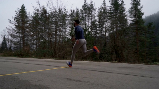 在森林里的柏油路上跟着一个男短跑运动员跑视频下载