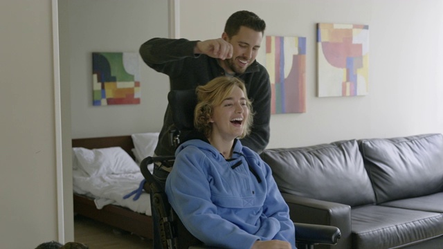 年轻夫妇在公寓客厅跳舞，女人坐在轮椅上。视频下载