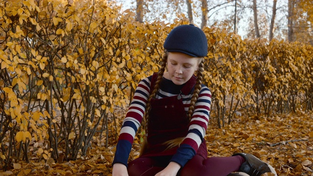可爱的少女红发辫在秋天的公园抛黄叶。快乐的女孩在公园里从秋天的树上扔落叶。快乐的女孩在秋天的金色公园里玩耍。视频下载