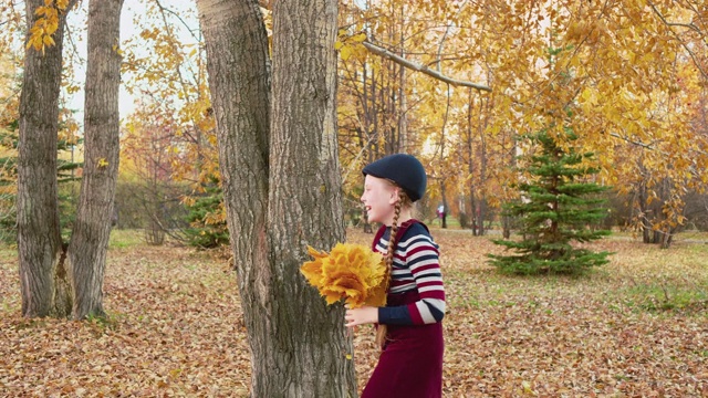 无忧无虑的女孩在秋天的公园里抛出黄色的枫树花束。在秋天的公园里，微笑的女孩从落叶上接过一束花。快乐的少女享受秋天的假期散步。视频下载