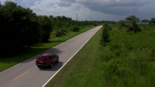 一辆运动型多用途车行驶在乡间小路上，经过一片翠绿的田野。视频下载