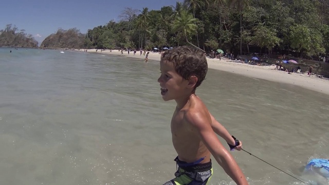 快乐的小男孩跑着跳进了海水里。夏天的乐趣/慢动作视频下载
