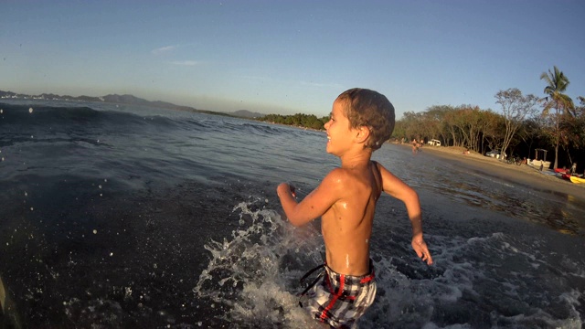 快乐的小男孩跑着跳进了海水里。夏天的乐趣/慢动作视频下载