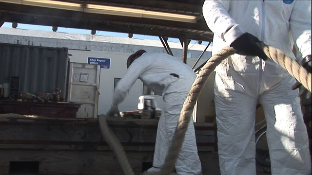 两名工人将一根大绳子从机械滑轮上滚下来。视频素材