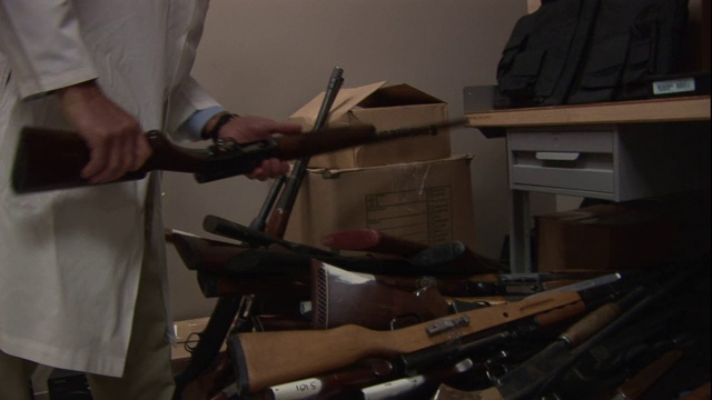 一位法医学家走进一个房间，从一堆东西中拿出一支步枪。视频素材