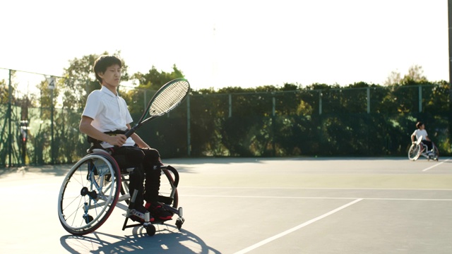 一个坐在轮椅上打网球的少年的中景视频下载