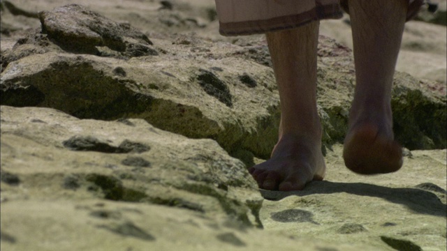 一个探险家赤脚在海滩上行走。视频素材