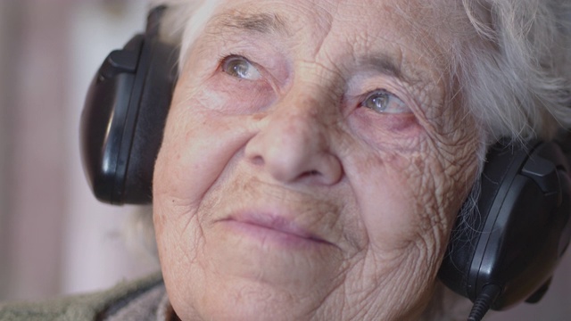 一个老年人听音乐与一套耳机和电话，娱乐，特写拍摄肖像的祖母，皱纹，享受音乐，随着节奏跳舞，乐趣。视频下载