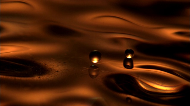 青铜液滴在波动的青铜液体上弹跳。视频素材