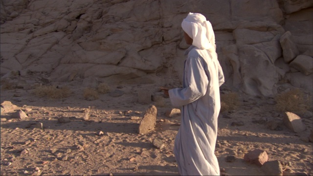 一个贝都因人在山脚下捡起两块石头。视频下载