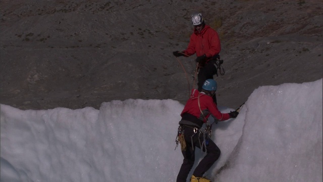 一名登山者帮助队友到达被冰雪覆盖的悬崖顶端。视频素材