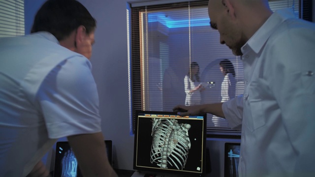 在控制室，医生和放射科医生一边看程序一边讨论诊断，在后台病人正在接受MRI或CT扫描程序。视频素材