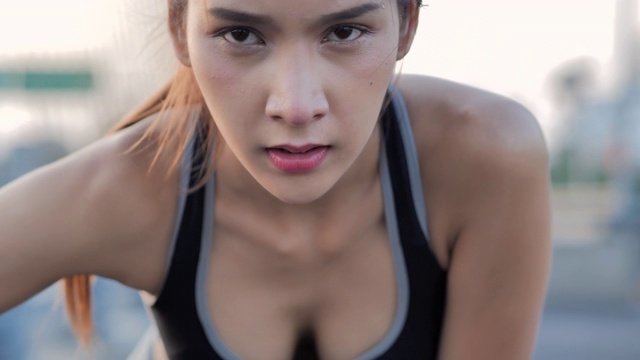 疲惫的肌肉发达的亚洲女性抬起头，看着镜头。她浑身是汗，试图喘口气，保持社交距离以防止冠状病毒或Covid-19的流行。视频素材