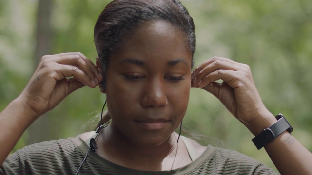 慢。铜。女运动员戴上耳塞，检查智能手表，准备在森林里跑步视频下载