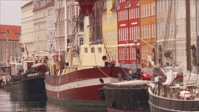 在哥本哈根，五颜六色的公寓大楼耸立在一条运河上，运河上停靠着许多船只。视频素材
