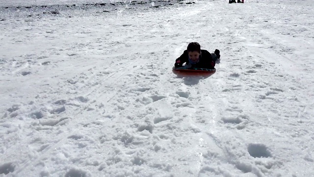 男孩滑下雪橇-冬天，雪山，白天。缓慢的运动。视频下载