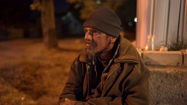 一个可怜的无家可归的人晚上坐在街上。视频素材