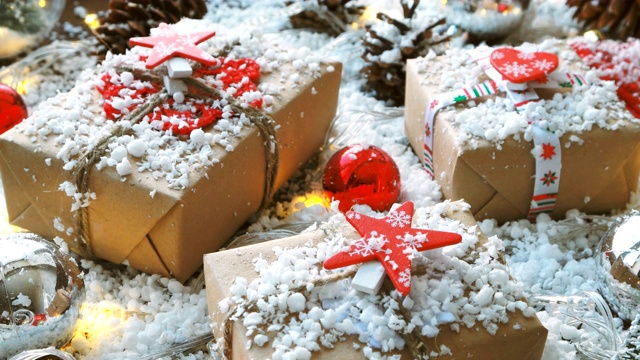 圣诞节和新年的背景与礼物，丝带，球和不同的装饰上的雪。用牛皮纸包装的礼物，上面有红星和心形图案。视频下载