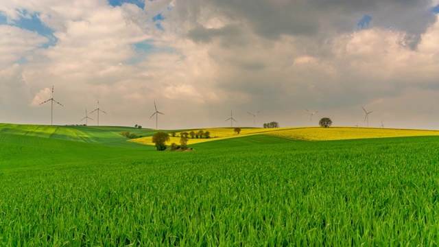 T/L Cloudscape在绿色的田野上，风力涡轮机在远处旋转视频素材