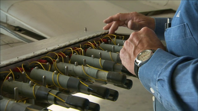 一个机械师抬起飞机机翼上的整流罩，检查照明弹架上的电线。视频素材