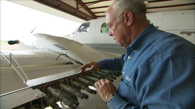 一个机械师抬起飞机机翼上的整流罩，检查照明弹架上的电线。视频素材