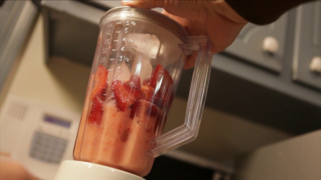 一个男人把水果和冰放在搅拌机里做冰沙。视频素材