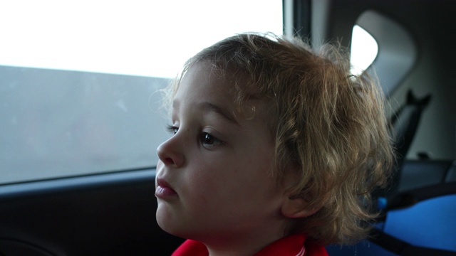 一个小男孩坐在车后座上望着窗外视频素材