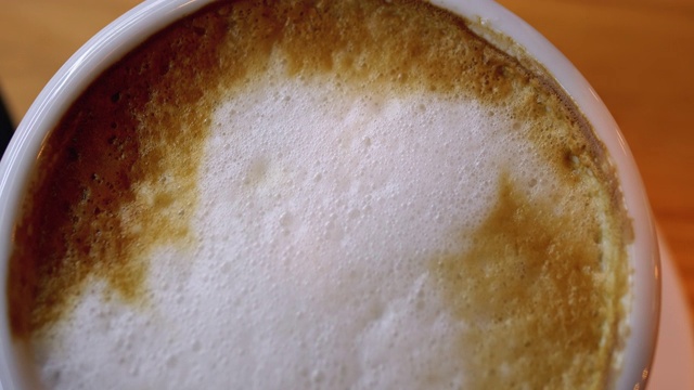 餐厅木桌上的一杯白色泡沫卡布奇诺。特写镜头视频素材