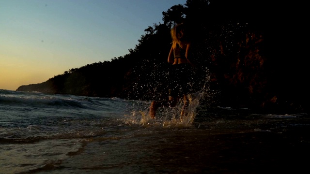 美丽的年轻女子在海滩上的波浪中奔跑视频素材