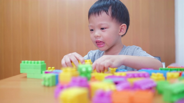 可爱的小亚洲3 - 4岁的蹒跚学步的男孩在家里玩五颜六色的塑料积木视频下载