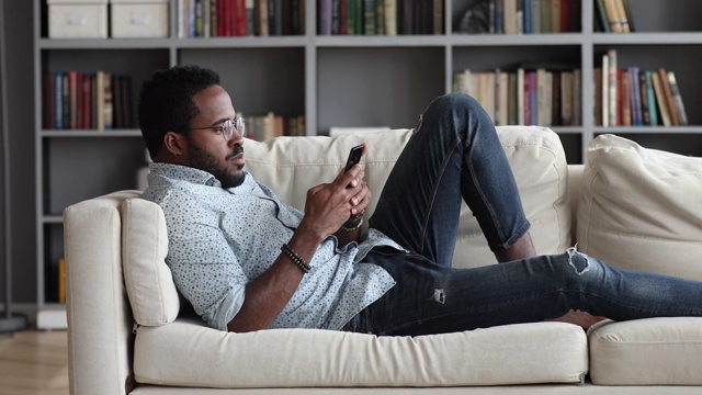 年轻的非洲人用电话放松在家里的沙发上视频素材