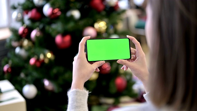 在圣诞树旁拿着彩色按键屏幕智能手机的女人视频素材